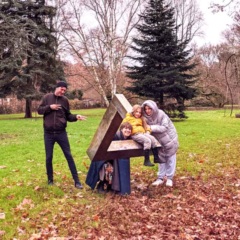 A family gathers around a wooden Penrose triangle found in a forest.